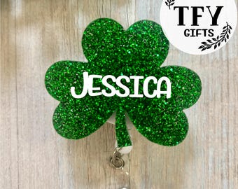 May include: Green glitter shamrock with the name Jessica on it. The shamrock is attached to a retractable badge holder. The badge holder is white with a silver clip. The shamrock is a popular symbol of Ireland and St. Patrick's Day.