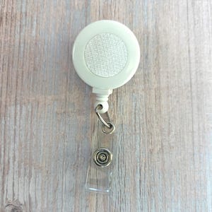 May include: White retractable badge reel with a clear plastic badge holder. The reel has a white fabric-like surface.