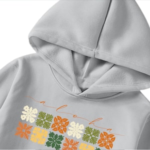 Puede incluir: Una sudadera con capucha gris con un diseño floral y la palabra "aloha" escrita en cursiva.