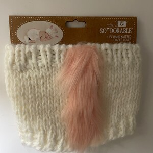 May include: White knitted diaper cover with a pink fur tail. The cover is made of soft, hand-knitted yarn and is perfect for newborn baby photoshoots. "So' Adorable" is printed on the packaging.