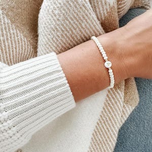 Peut inclure: Un bracelet en perles blanches avec un charme en or en forme de lettre 'A'.