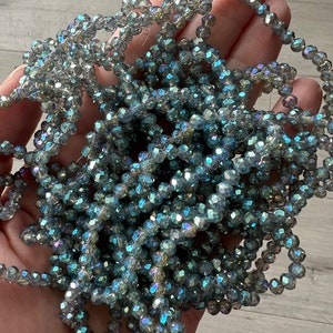 May include: A strand of iridescent blue faceted glass beads. The beads are small and round, and they have a shimmery finish.