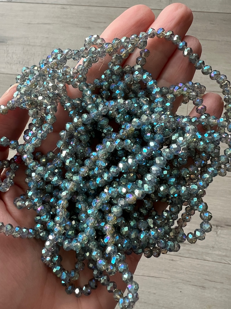 May include: A strand of iridescent blue faceted glass beads. The beads are small and round, and they have a shimmery finish.