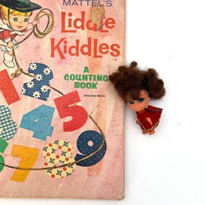 May include: A vintage Whitman Big Tell-a-Tale Mattel's Liddle Kiddles A Counting Book with a pink cover featuring a cartoon character and colorful numbers, accompanied by a small doll with brown hair wearing a red dress and gold trim.