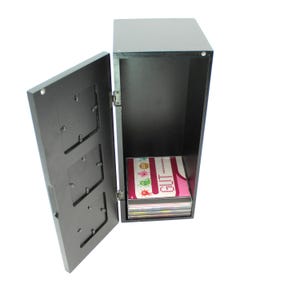 May include: A dark gray, rectangular cabinet with an open door revealing a stack of colorful items. The door has three rectangular cutouts. The cabinet is on a white background.