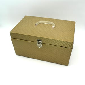 May include: A gold-colored, rectangular storage box with a silver handle and latch. The box has a quilted pattern on the lid.
