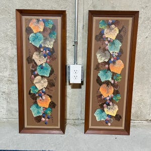 May include: Two framed paintings with a brown background and a vertical design of colorful leaves and grapes. The frames are brown wood.