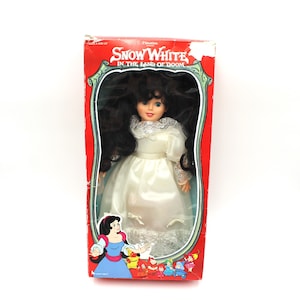May include: A vintage Snow White doll in a white dress with a lace trim. The doll has long black hair and blue eyes. The doll is packaged in a red box with the words "Snow White in the Land of Doom" printed on it.