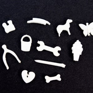 May include: A set of white plastic figurines, including a bucket, a wrench, a bone, a horseshoe, a heart, a butterfly, a horse, a pair of scissors, and a cone with a swirl on top.