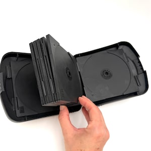 May include: A black multi-disc storage case with a hinged design, featuring a central leaf that holds multiple discs. The case is open, revealing empty circular disc compartments with central hubs, constructed from durable black plastic material.