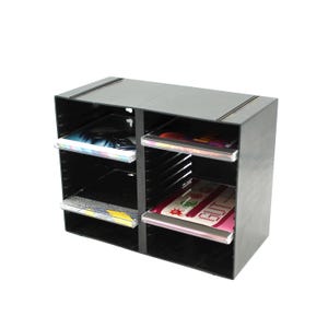 May include: A black, multi-compartment storage unit with clear shelves. The unit is filled with various colorful items, including books and magazines. The unit is designed to hold and organize items.