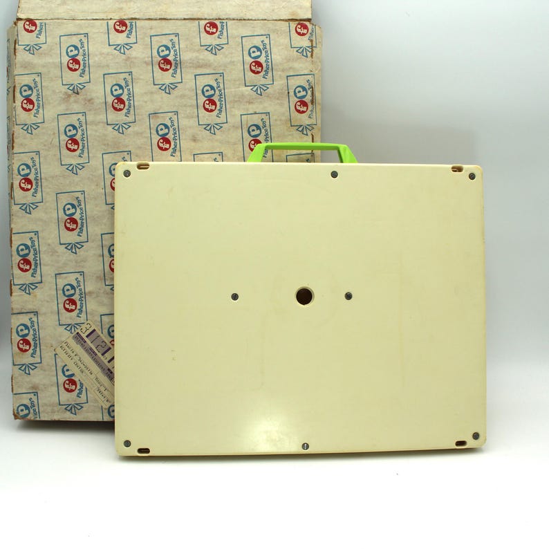 May include: The bottom of a white plastic toy with a green handle. The toy has a round hole in the center and four small holes around the edges.