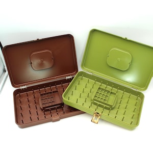 May include: Two open plastic storage boxes. One is brown, the other is green. Both have a rectangular shape with a hinged lid and a latch. The interior of each box has a grid of small pegs and a central raised section.