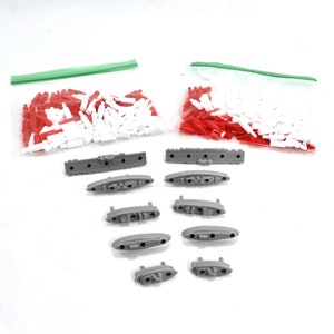 May include: Two bags of red and white plastic game pieces, and ten gray plastic game pieces shaped like ships. The ships are in various sizes and have different numbers of cannons.