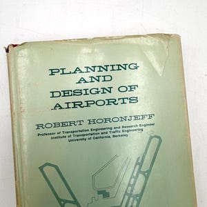May include: A vintage book titled "Planning and Design of Airports" by Robert Horonjeff. The cover is a faded green with black text and a diagram of an airport runway. The book is slightly worn, showing signs of age.