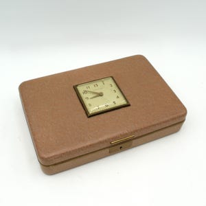 May include: A vintage, light brown, rectangular box with a brass latch and a small, round, white clock face with black hands and black Roman numerals. The clock face is set into the top of the box.