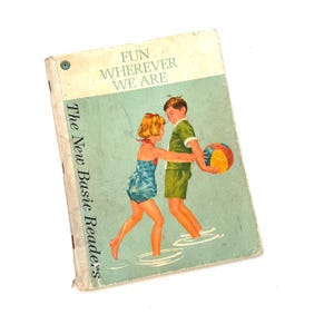 May include: Vintage children's book titled "The New Basic Readers" with the cover art of two children playing with a beach ball. The book cover has the text "FUN WHEREVER WE ARE" in white letters.