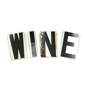 May include: The word "WINE" spelled out in black letters on white rectangular tiles.