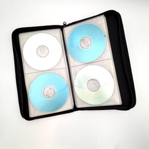 May include: A black zippered storage case containing four circular discs held in clear plastic sleeves. The discs are solid colors, including one white, two light blue, and one pale green, each featuring a central hole and a small printed label.