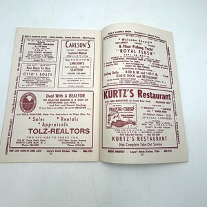 May include: Open magazine pages featuring advertisements for restaurants, seafood, and real estate services. The pages display text and illustrations in a vintage style, with a focus on local businesses and services.