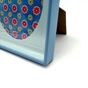 May include: A pale blue picture frame with a white mount and a patterned design. The design features red and yellow floral patterns on a blue background. The frame is made of wood and has a clean, modern appearance.