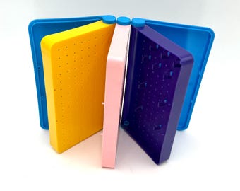 May include: A multi-colored plastic storage organizer featuring a series of hinged, rectangular compartments in yellow, light pink, and deep purple. The unit includes a blue base and lid, with each section containing a grid of small, evenly spaced holes.
