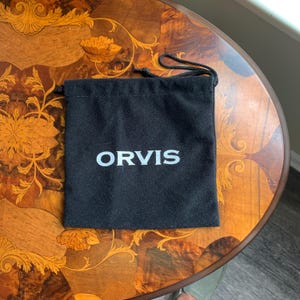 May include: A black drawstring bag with the word "ORVIS" embroidered in white on the front.
