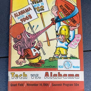 May include: A vintage Tech vs. Alabama souvenir program from November 14, 1964, featuring a colorful cartoon illustration of two mascots. One mascot holds a football labeled Today's Rubber Game, while signs in the background read Alabama Won In 1963 and Tech Won In 62.