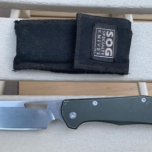 Könnte beinhalten: Ein grünes und silbernes Klappmesser mit einer schwarzen Scheide. Die Scheide trägt den Text "SOG SPECIALTY KNIVES INC.".