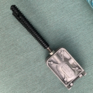 Op de afbeelding: Een zilveren metalen mal met een zwarte schroefdraadstang eraan bevestigd. De mal heeft de tekst "GILTS MOLDS  SURBANK CA  61502" erop.