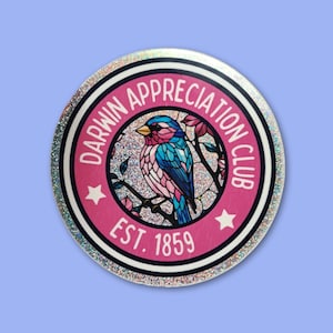 May include: A pink and silver glitter sticker with a white circle and black text that reads "Darwin Appreciation Club Est. 1859". Inside the circle is a stained glass style bird with blue, pink, and white colours.