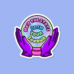 May include: A sticker showing a crystal ball held by purple gloved hands. The crystal ball has a rainbow effect and the text "May the stars be in your favour" in a playful font. The sticker has a white border and is on a light blue background.