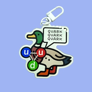 May include: A white keychain with a cartoon duck and the words "Quark Quark Quark" on a white speech bubble. The duck has a blue, red, and green circle on its body.
