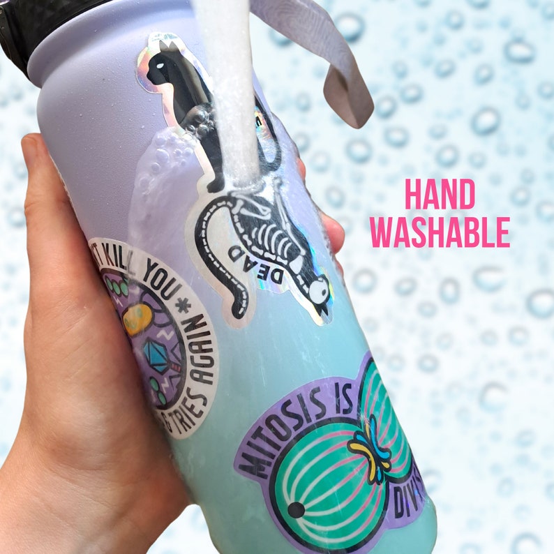 May include: A light blue reusable water bottle with various stickers, including a skeleton, a cat, and a graphic that says "It Kill You* Tries Again". The bottle is being rinsed under a stream of water. The text "HAND WASHABLE" is visible in the background.