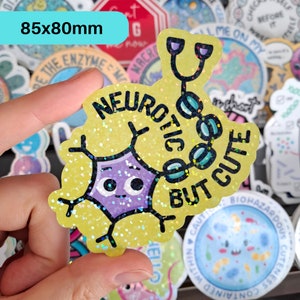 May include: A yellow glitter sticker featuring a cartoon neuron with a purple body and a stethoscope. The text "Neurotic But Cute" is written around the neuron.