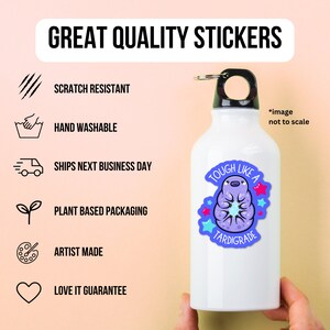 May include: A white water bottle with a black lid and a sticker of a purple tardigrade with the text "Tough Like A Tardigrade". The sticker has a blue background with pink stars. The bottle is on a white background.