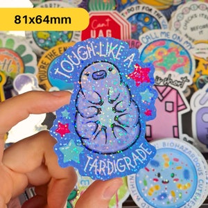 May include: A blue and pink glitter sticker with a cartoon tardigrade, a microscopic animal, and the text "Tough Like A Tardigrade".