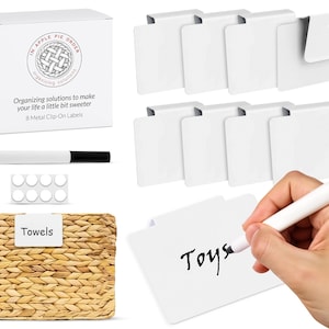 May include: A set of eight white metal clip-on labels with a black dry-erase marker and a pack of adhesive dots. The labels are blank and can be used to label containers, bins, or other items. The labels are shown in the image with the words "Towels" and "Toys" written on them.