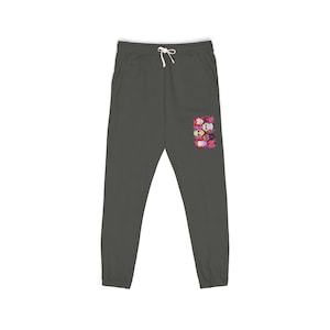 May include: Dark gray sweatpants with a drawstring waist and a small graphic of colorful cartoon faces on the right leg. The sweatpants have two pockets and a relaxed fit.