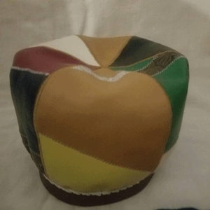 May include: A patchwork leather hat featuring a variety of colors including brown, yellow, green, white, and burgundy. The hat has a rounded crown and a dark brown brim. The hat is made of stitched leather pieces.