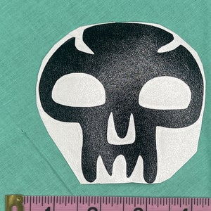 May include: Black and white skull sticker with a textured surface. The sticker is approximately 2 inches wide.