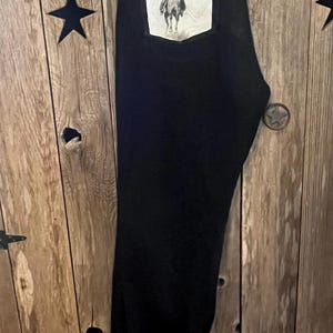 May include: Black denim jeans with a white patch pocket featuring a black and white image of a person riding a horse.