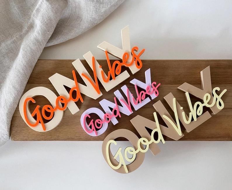 Pode incluir: Recortes de madeira que dizem "Good Vibes Only" em v&aacute;rias cores. As palavras est&atilde;o em uma mistura de fontes e cores, incluindo laranja, rosa e amarelo. Os recortes s&atilde;o dispostos em uma superf&iacute;cie de madeira.