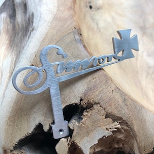 Könnte beinhalten: Ein silberner Metalls Schlüssel mit der Gravur "Simmons". Der Schlüssel hat einen kreuzförmigen Kopf.