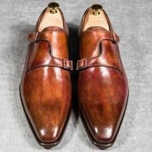 May include: A pair of brown leather monk strap shoes with a pointed toe and a polished finish.