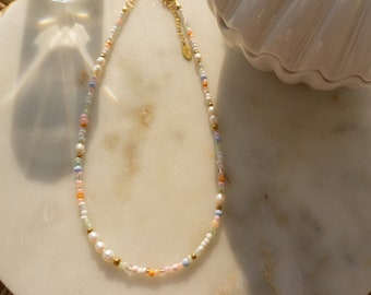 May include: A delicate gold chain necklace with small white pearls and colorful beads. The necklace is on a white marble surface.