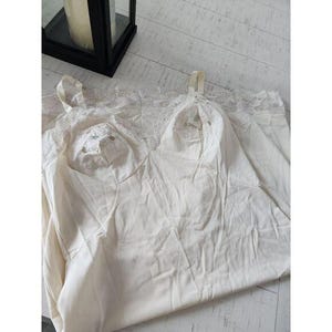 May include: Ivory-colored slip with delicate lace trim along the neckline and straps. The slip features a subtle sheen and a soft, flowing fabric. The garment has a classic, vintage aesthetic.