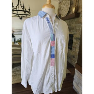 May include: White button-down shirt with a colourful striped accent down the front. The accent features blue, red, green, and pink stripes. The shirt is displayed on a mannequin.