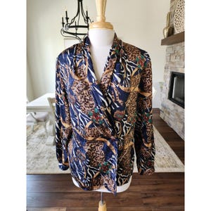 May include: A long-sleeved blouse with a wrap-style front, featuring a bold animal print. The print combines leopard spots, zebra stripes, and gold chain accents on a navy blue background. Red and green floral details add a pop of color.