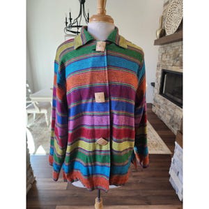 May include: A long-sleeve button-down jacket featuring horizontal stripes in vibrant shades of green, blue, orange, purple, and red. The garment includes a classic collar and three large, square-shaped light-colored wooden buttons down the front.